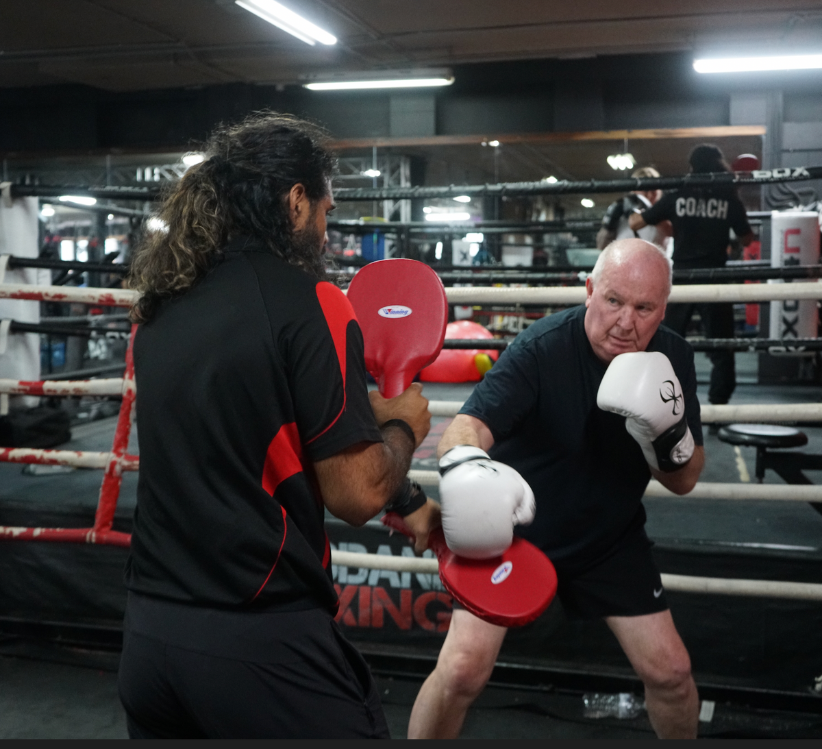 A boxer wearing green gloves practising punches with a pad holder at Brisbane Boxing.