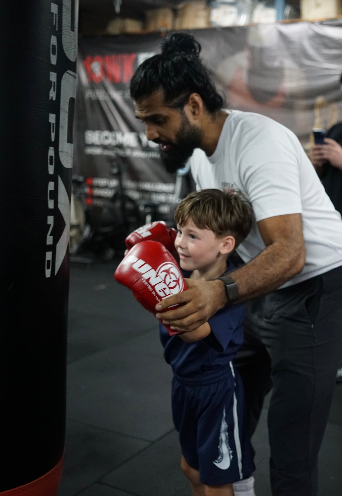 A Brisbane Boxing coach giving instructions to a group of young boxers in headgear and Team Brisbane Boxing kit beside the ring.